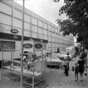 przeszklona hala wystawowa, przed nią samochody osobowe i spacerujący ludzie