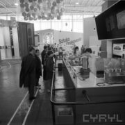 stoiska w hali wystawowej, między nimi zwiedzający ludzie