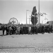 duża grupa ludzi stoi na terenie targów, za nimi ażurowa konstrukcja kuli ziemskiej i maszty z flagami państw