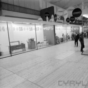 stoisko w hali wystawowej, zwiedzający ludzie, u sufitu wiszą okrągłe reklamy firm