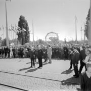 duża grupa ludzi, za nimi ażurowa konstrukcja kuli ziemskiej i maszty z flagami państw