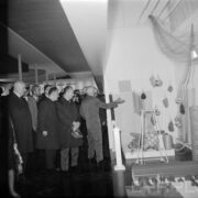 grupa mężczyzn, część w płaszczach, w hali wystawowej