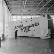 stoiska w hali wystawowej, przed jednym z nich stojący mężczyzna