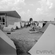 rozstawione namioty różnej wielkości na trawie, zwiedzający ludzie, z lewej fragment budynku ze skośnym dachem