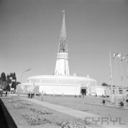 okrągły budynek z ażurową iglicą na dachu, na placu spacerujący ludzie