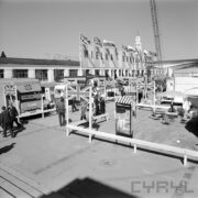 plac przed murowanym budynkiem, na placu samochody, autobusy, reklamy, zwiedzający ludzie