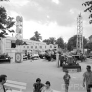 traktory, maszyny, urządzenia, samochody na betonowym placu, w głębi z lewej przeszklona hala