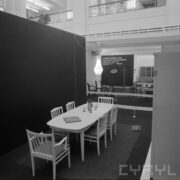 stoisko ze stołem i stojącymi wokół niego krzesłami w hali wystawowej