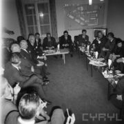 grupa mężczyzn i kobiet siedząca przy stołach, na stołach szklanki, kieliszki, butelki i talerze