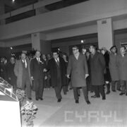 duża grupa mężczyzn w płaszczach, wśród nich jedna kobieta, w hali wystawowej