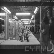 stoiska z lalkami w hali wystawowej, przy nich zwiedzający ludzie