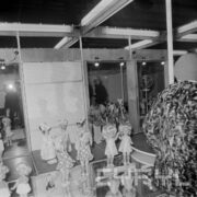 stoisko z lalkami w hali wystawowej, przy nich zwiedzający ekspozycję ludzie