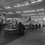 stoiska w hali wystawowej, przy nich stoją ludzie i oglądają ekspozycję