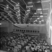 duża liczba osób siedzi na krzesłach ustawionych w układzie amfiteatralnym, w głębi przy mównicy mężczyzna