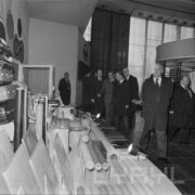 grupa mężczyzn, część w płaszczach, ogląda ekspozycję w hali targowej