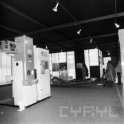 stoiska z urządzeniami w hali wystawowej, w głębi kilka osób