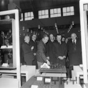 grupa mężczyzn, część w płaszczach ogląda ekspozycję w hali targowej