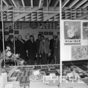 grupa mężczyzn, część w płaszczach ogląda ekspozycję w hali targowej