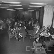 grupy kobiet i kilku mężczyzn siedzi przy stolikach, na których przygotowano poczęstunek