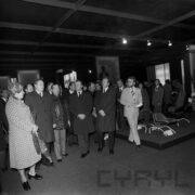 grupa mężczyzn (część w płaszczach) i kilka kobiet w hali wystawowej