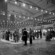 stoiska w hali targowej z odzieżą prezentowaną na manekinach, na pierwszym planie dwie kobiety oglądają ekspozycję