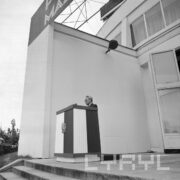 mężczyzna stoi przy mównicy przyozdobionej polską flagą z orłem i przemawia