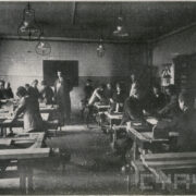 grupa uczniów z dwoma nauczycielami stojąca przy stołach i heblująca drewno