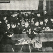 grupa uczniów z dwoma nauczycielami siedząca przy stołach; część uczniów gra w szachy, część majsterkuje