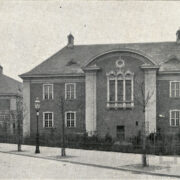 duży budynek z cegieł, przed budynkiem widoczne świeżo posadzone drzewa