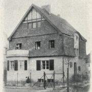 piętrowy, otynkowany dom z owalnym wykuszem i spadzistym dachem pokrytym dachówką i użytkowym poddaszem