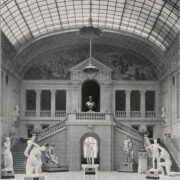 liczne rzeźby przestawiające ludzi na tle schodów i ścian zdobionych malowidłami; u góry przeszklony sufit, na którym wisi lampa